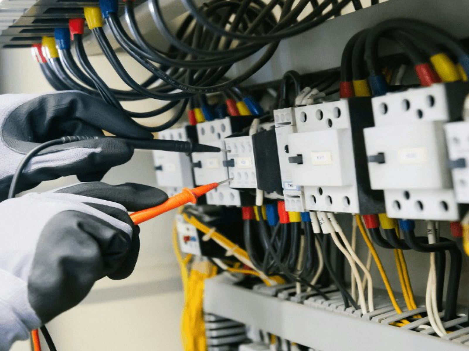 Electrician testing wiring inside a switchboard with a multimeter