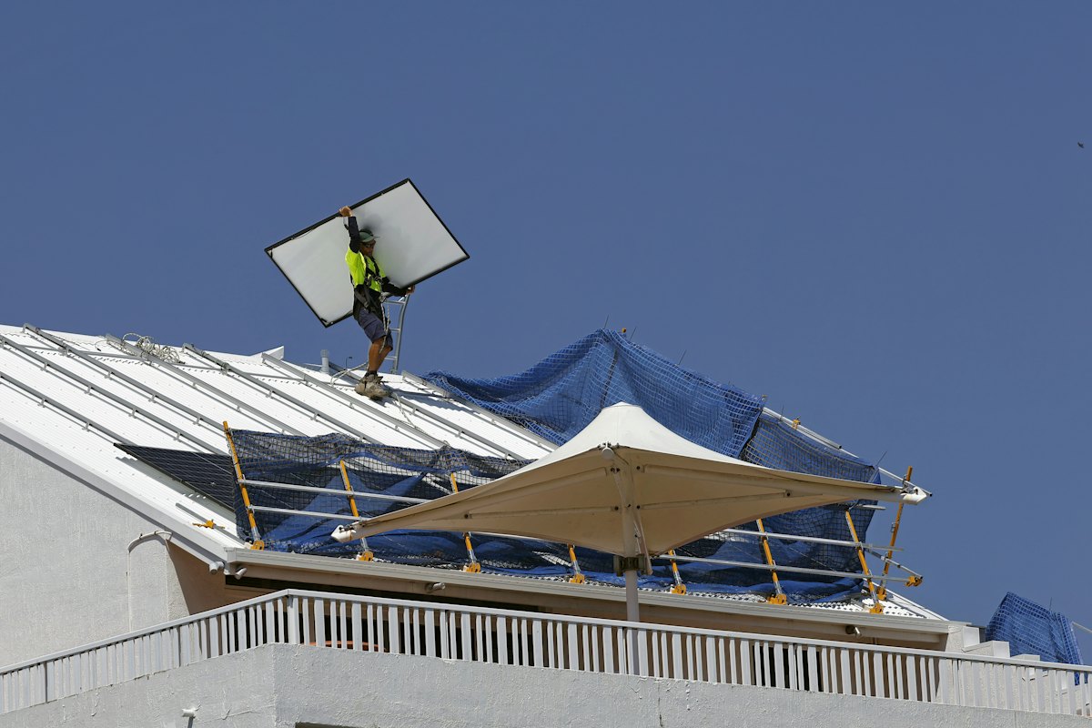 Worker carrying a solar panel across a roof